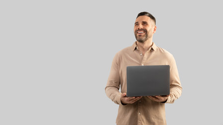 Positive confident middle aged businessman holding in hand opened laptop computer and looking at free space, panoramaの写真素材