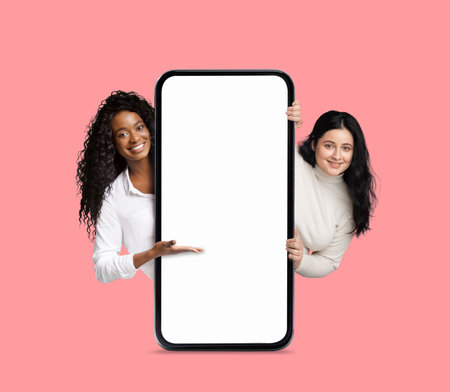 Great App. Cheerful Multiethnic Females Pointing At Big Blank Smartphone Screenの写真素材