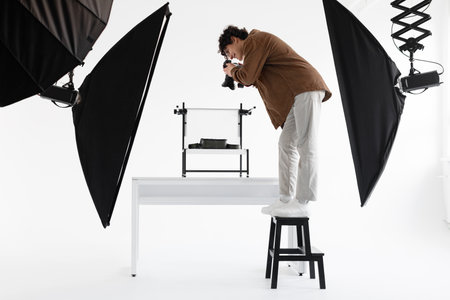 Professional male photographer standing on ladder and taking high angle content photos, working at professional studioの写真素材