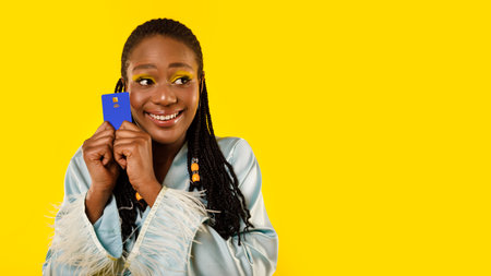 African Lady Holding Credit Card Looking Aside Over Yellow Backgroundの写真素材