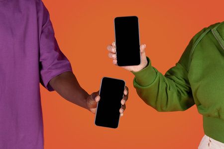 Cropped of multiracial couple holding phones with blank screens