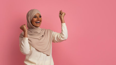 Overjoyed muslim woman celebrating success, shaking fists and looking asideの写真素材