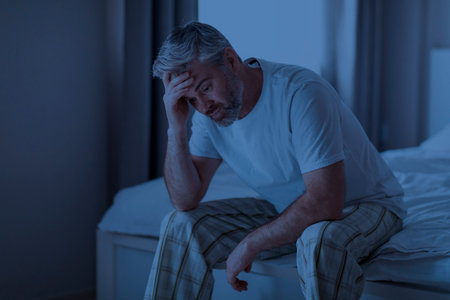 Sleepless middle aged man sitting on bed at homeの写真素材