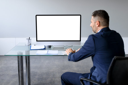Rear view shot of businessman looking at blank computer monitor, watching webinar or having online...
