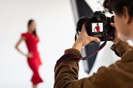 Professional male photographer and beautiful female model in red dress making beauty or content photoshoot in studioの写真素材