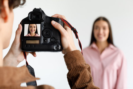 Photographer taking portrait of young beautiful woman in photostudio, focus on working digital camera during photoshootの写真素材