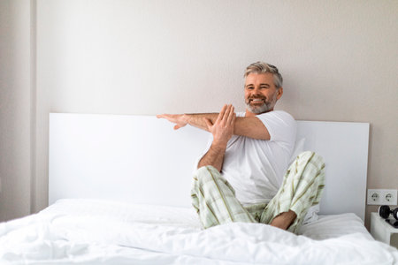 Joyful mature man sitting in bed, stretching arms, copy spaceの写真素材