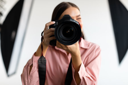 Young woman with dslr camera photographing in studio with lighting equipment, taking pictures with professional cameraの写真素材