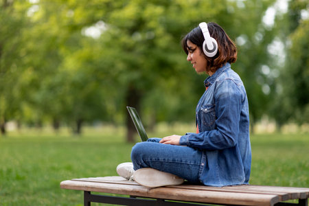 Happy Young Arab Woman In Wireless Headphones Using Laptop Outdoorsの写真素材