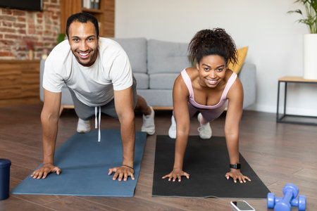 Sport and fitness for muscle at home. Glad young black couple in sportswear do plank on hands on floorの写真素材
