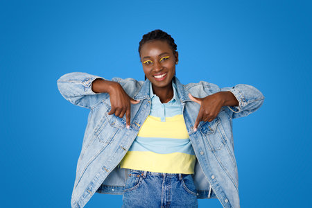 Smiling pretty young black woman pointing down on blueの写真素材