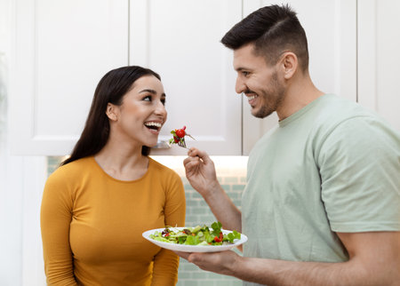 Happy handsome man feeding his pretty girlfriend with saladの写真素材