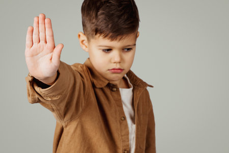Sad caucasian 6 years old little boy show stop gesture with hand isolated on gray studio background, close upの写真素材
