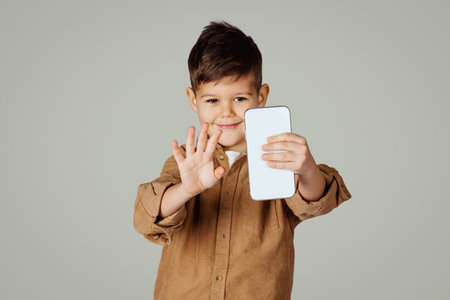 Cheerful caucasian 6 years old little boy waving hand on smartphone, has video callの写真素材