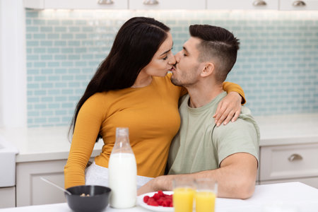 Young couple kissing while having breakfast together at homeの写真素材