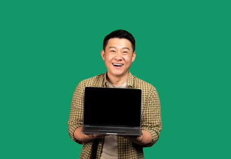 Happy asian middle aged man showing laptop computer blank screen, recommending great website, green background, mockupの写真素材