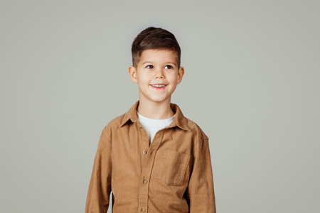 Smiling caucasian 6 years old little boy pupil in casual looks at empty space isolated at gray studio backgroundの写真素材