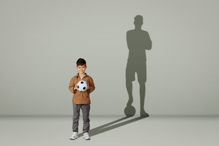 Happy caucasian 6 years old little kid in casual with soccer ball and shadow of adult soccer playerの写真素材