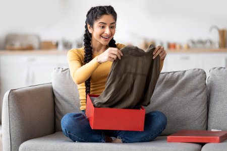Happy Young Indian Woman Unboxing Parcel With New Clothes At Homeの写真素材