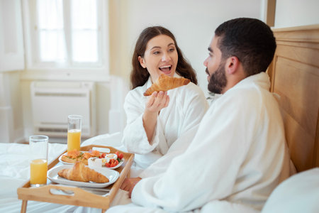 Wife Feeding Husband Giving Croissant Having Breakfast In Bed Indoorの写真素材