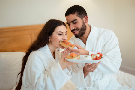 Husband Feeding Wife Giving Her Sandwich Having Breakfast In Bedroomの写真素材