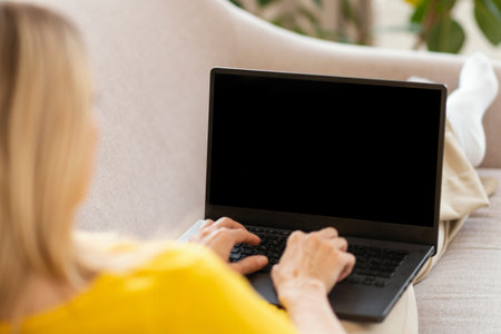 Millennial caucasian blonde lady in yellow clothes typing on computer with blank screenの写真素材