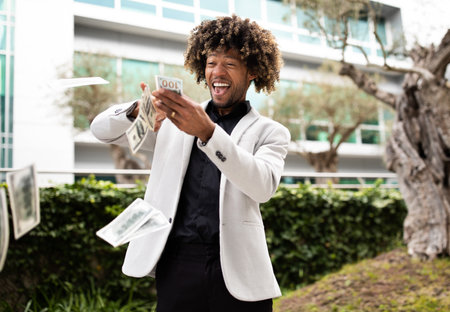 Overjoyed black middle aged businessman throwing money away showing his wealthiness, standing outdoors, free spaceの写真素材