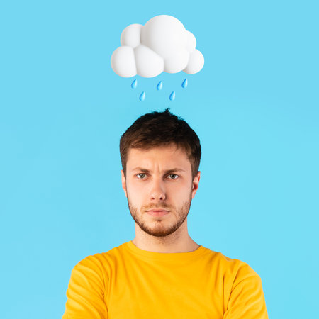 Unhappy young european man with abstract cloud and rain sign above head isolated on blue studio backgroundの写真素材