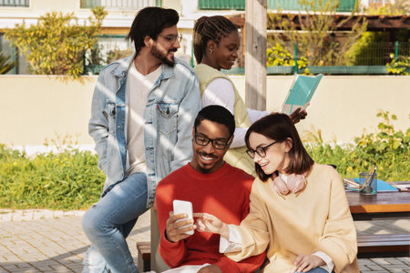 Glad millennial multiethnic modern students look at smartphone, have video call, study togetherの写真素材