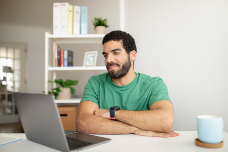 Smiling handsome millennial arabic man with beard has video call, working with laptop at workplace...