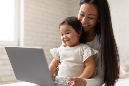 Happy Asian Mom And Little Baby Daughter Using Laptop Indoorの写真素材