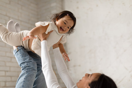 Korean Mommy Playing With Little Daughter Riding On Legs Indoorの写真素材