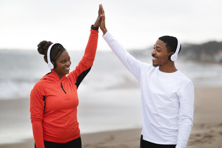 Cheerful millennial african american couple in sportswear and headphones giving high five, celebrating great runの写真素材