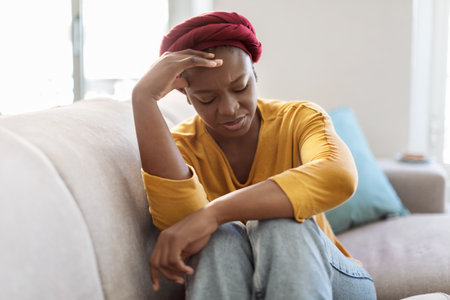 Upset black woman sitting on couch at home, cryingの写真素材