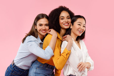 Girls friendship concept. Portrait of three happy diverse women posing and smiling at camera over pink backgroundの写真素材