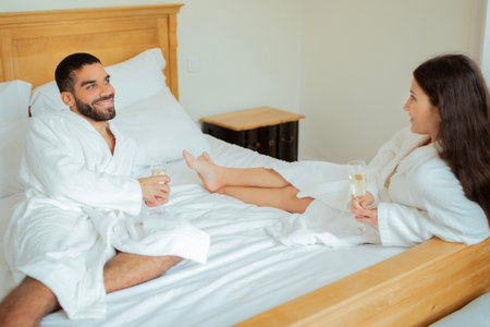 Married Couple Drinking Champagne Lying In Bed In Hotel Suiteの写真素材