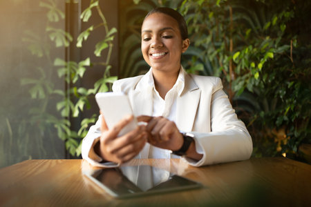 App for business chat. Happy millennial african american businesswoman in white suit chatting on smartphoneの写真素材
