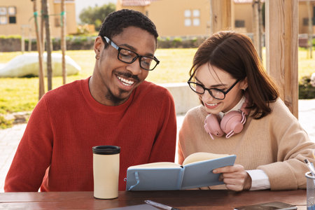 Smiling millennial black man and european lady modern students read books, study together at universityの写真素材