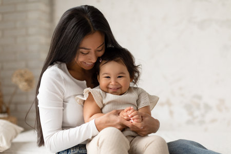 Happy Japanese Mommy Cuddling With Toddler Baby Daughter At Homeの写真素材