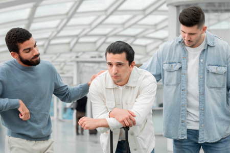 Guys Supporting Friend Having Problem Standing With Suitcase In Airport