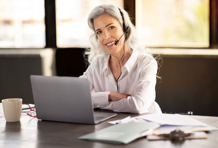 Cheerful Businesswoman Wearing Headset Communicating Online At Laptop In Officeの写真素材