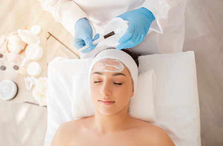 Beauty Treatments. Cosmetologist applying nourishing mask on indian woman face at spa salon,の写真素材
