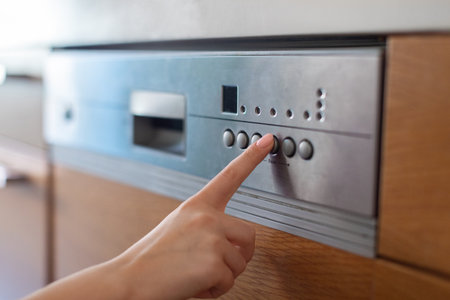 Unrecognizable female turning on dishwasher machine in kitchen