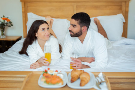 Couple Enjoying Breakfast Lying In Bed Near Tray In Hotelの写真素材