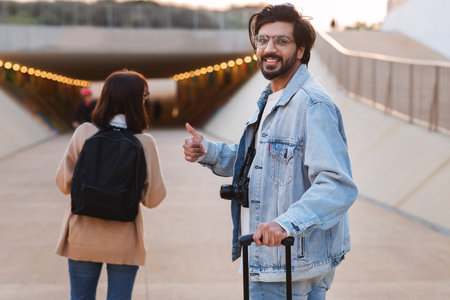 Smiling millennial indian male with suitcase show thumb up sign, caucasian lady tourist waiting for taxiの写真素材