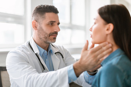 Friendly middle aged male doctor checking sore throat or thyroid glands, touching neck of young female patientの写真素材