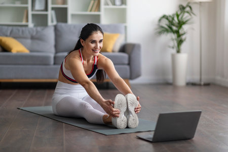 Beautiful young woman have workout at home, using laptop