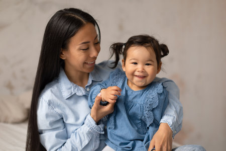 Cheerful Japanese Mommy And Adorable Baby Daughter Posing At Homeの写真素材