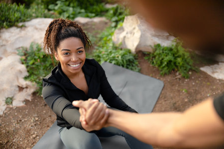 Millennial african american man helping to pretty wife get up from mat, enjoy workout in morning
