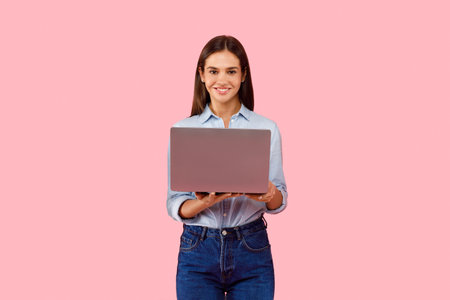 Portrait of smiling caucasian lady holding and using laptop computer isolated over pink studio...